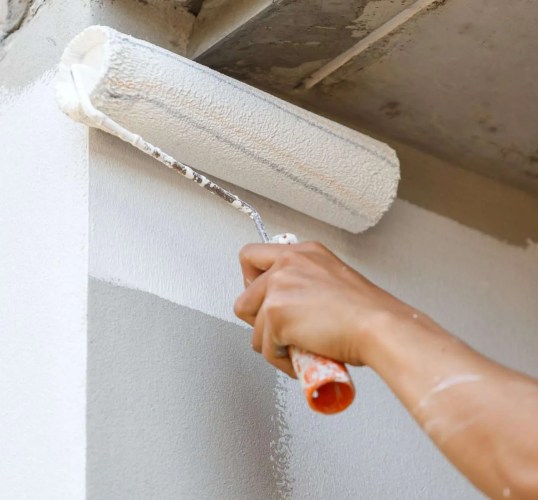 A person painting a wall with a paint roller.