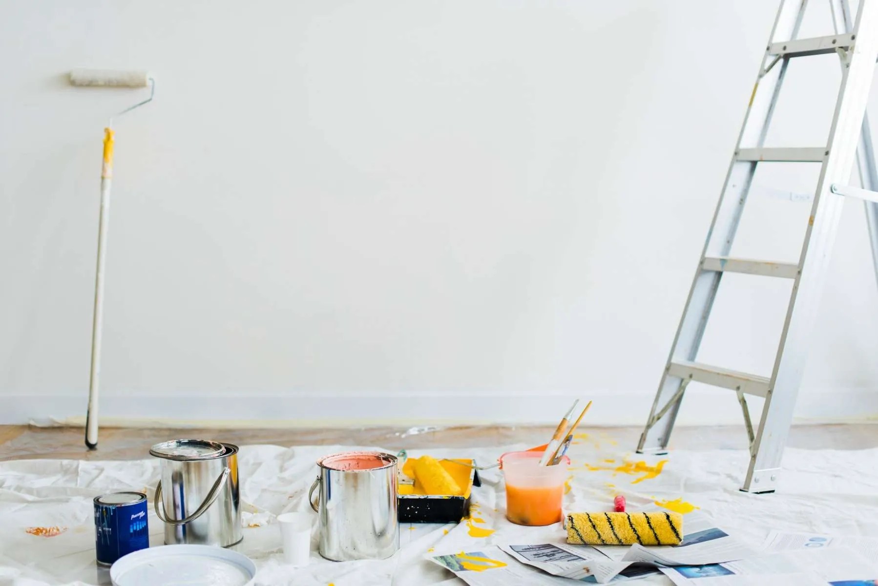 A room with paint brushes, paint, and a ladder.